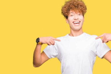 Afro saçlı genç yakışıklı adam rahat beyaz t-shirt giyen yüzünde gülümseme ile emin görünümlü, parmakları gururlu ve mutlu kendini işaret.