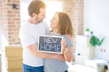 Orta yaş Senior çift yeni bir eve hareket, yeni bir ev metin ile bir tahta tutan Apartmant aşık mutlu gülümseyen