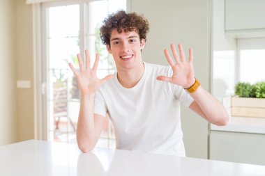 Genç yakışıklı adam evde gösteren beyaz t-shirt giyen ve parmakları ile işaret on numara emin ve mutlu gülümserken.