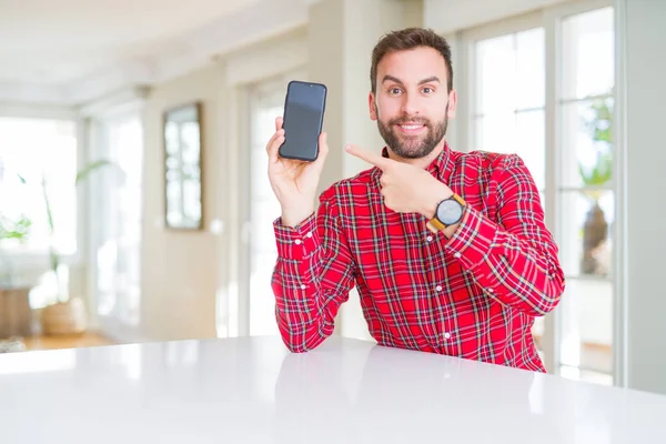Przystojny Człowiek Pokazując Smartphone Ekran Bardzo Szczęśliwy Wskazując Ręką Palcem — Zdjęcie stockowe