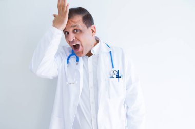 Orta yaş doktor adam beyaz arka plan üzerinde stetoskop ve tıbbi ceket giyen hata için kafasına el ile şaşırttı, hata hatırlıyorum. Unuttum, kötü bellek kavramı.