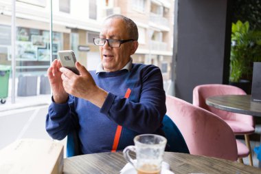 Mutlu ve zevk rahatlatıcı smartphone kullanarak emeklilik gülümseyen restaurante, kahve içme yakışıklı orta yaş komuta sizde