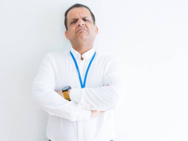 Orta yaş iş adamı beyaz arka plan üzerinde kimlik kartı giyen şüpheci ve sinirli, çapraz kolları ile yüzünde onaylamayan ifade. Negatif kişi.