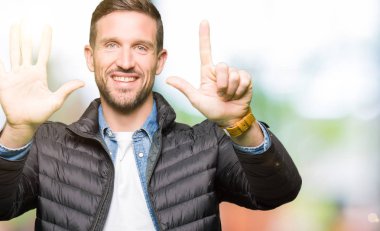 Kış ceket gösterme ve parmakları ile işaret giyen yakışıklı adam kendinden emin ve mutlu gülümseyerek süre yedi numara.