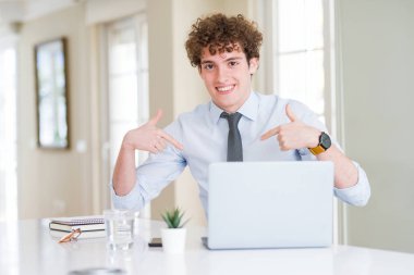 Ofiste bilgisayar dizüstü bilgisayar ile çalışan genç iş adamı yüzünde gülümseme ile emin görünümlü, parmakları gururlu ve mutlu kendini işaret.