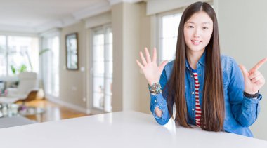 Uzun saçlı genç güzel asyalı kadın denim ceket gösteren ve parmakları ile işaret ederken emin ve mutlu gülümseyerek yedi numara.