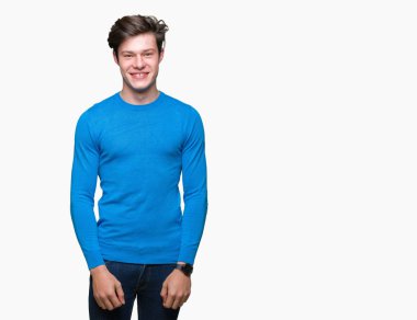 Genç yakışıklı adam yüzünde mutlu ve güzel bir gülümseme ile izole arka plan üzerinde mavi kazak giyiyor. Şanslı kişi.