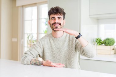 Beyaz masaüzerinde oturan rahat kazak giyen genç adam elleri büyük ve büyük boy işareti gösteren gesturing, ölçü sembolü. Kameraya bakarak gülümsüyor. Ölçme kavramı.