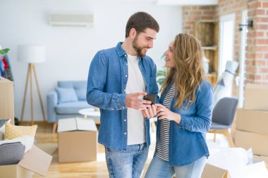 Genç çift karton kutular etrafında akıllı telefon kullanarak yeni bir eve hareket
