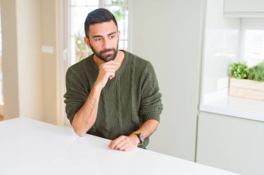 Çene düşünme hakkında soru, dalgın ifade üzerine el ile evde rahat kazak giyen yakışıklı İspanyol adam. Düşünceli yüzüyle gülümsüyor. Şüphe kavramı.