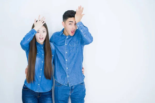 Beautiful young asian couple over white isolated background surprised with hand on head for mistake, remember error. Forgot, bad memory concept.