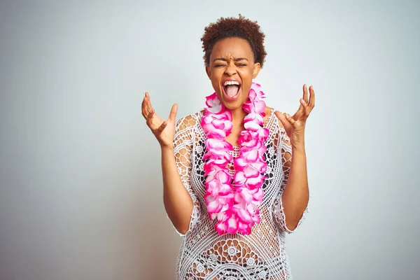 Young african american woman with afro hair wearing flower hawaiian lei over isolated background celebrating mad and crazy for success with arms raised and closed eyes screaming excited. Winner concept