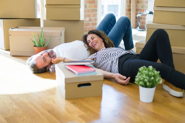 Middle age senior romantic couple lying on the floor, smiling happy for moving to a new house, relaxing and taking a break of packing boxes