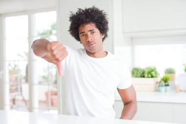 Evde oturan rahat beyaz tişört giyen genç afro-amerikan adam mutsuz ve kızgın görünümlü reddedilme ve başparmak aşağı jest ile olumsuz gösteren. Kötü ifade.