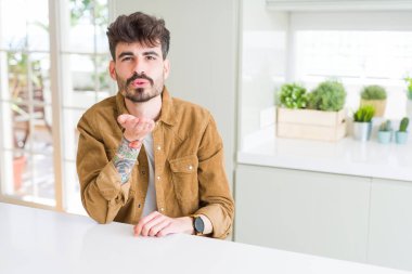 Beyaz masada oturan rahat ceket giyen genç adam güzel ve seksi olmak havada el ile bir öpücük üfleme kameraya bakarak. Aşk ifadesi.