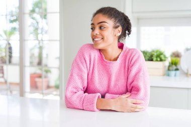 Afro saçlı güzel afro-amerikan kadın rahat pembe kazak giyen yüzünde gülümseme, doğal ifade ile yan bakıyor. Gülmekten emin.