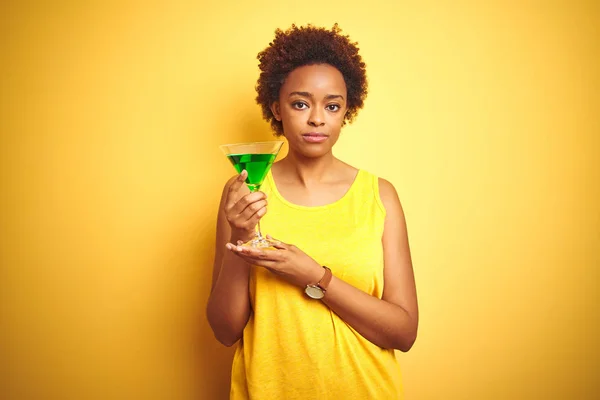 Young african american woman with afro hair drinking a cocktail over yellow isolated background with a confident expression on smart face thinking serious