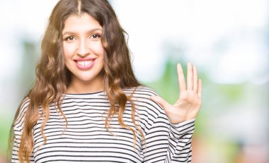 Kendinden emin ve mutlu gülümseyerek süre beş numara gösterilen ve parmakları ile işaret genç güzel kadın giyiyor çizgili süveter.