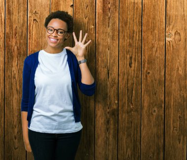 Genç güzel Afrikalı-Amerikalı kadın gözlük gösterilen ve parmakları ile işaret izole arka plan üzerinde kendinden emin ve mutlu gülümseyerek süre 5 numara.