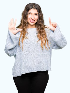 Gösterilen ve parmakları ile işaret genç güzel kadın giyiyor kış kazak kendinden emin ve mutlu gülümseyerek süre yedi numara.