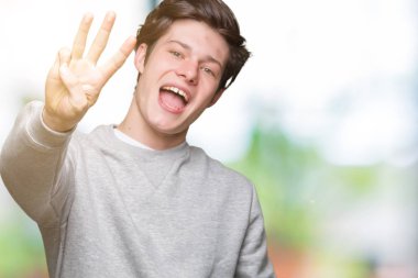 Gösterilen arka plan üzerinde sweatshirt giyen genç yakışıklı sportif adam izole ve parmakları ile işaret kendinden emin ve mutlu gülümseyerek iken üçüncü.