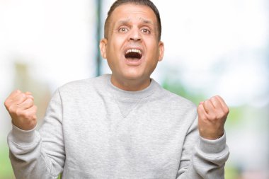 İzole arka plan kutlama üzerinde spor kazak giyen orta yaş Arap adam şaşırttı ve başarı için kaldırdı kollarını açarak hayret ve gözleri açık. Kazanan kavramı.