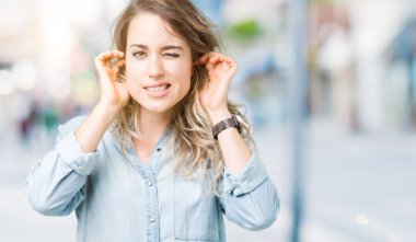 Güzel sarışın genç kadın parmakları ile yüksek sesle müzik gürültü rahatsız ifade kulaklarıyla kapsayan izole arka plan üzerinde. Sağır kavramı.