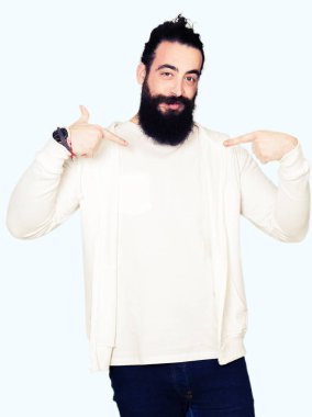 Uzun saç ve sakal yüzünde gülümseme ile kendinden emin görünüyorsun, kendini gururlu ve mutlu parmakları ile işaret sportif sweatshirt giyen genç adamla.