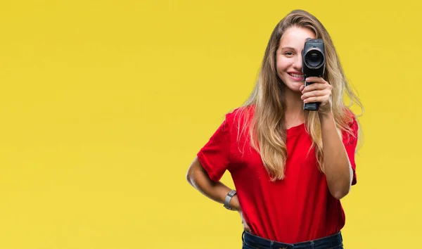 Young beautiful blonde woman filming using vintage camera over isolated background with a happy face standing and smiling with a confident smile showing teeth