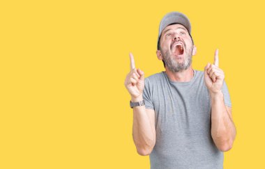 Yakışıklı orta yaş ağarmış komuta sizde Spor şapkası izole arka plan üzerinde hayret ve yukarıya bakıp parmakları ile işaret şaşırttı ve silah kaldırdı.