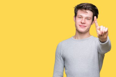 Ve parmak gülümseyen süre bir numara ile kendinden emin ve mutlu yukarıyı gösteren izole arka plan üzerinde kış kazak giyen genç yakışıklı adam.