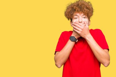 Kırmızı t-shirt giyen afro saç ile genç yakışıklı adam yanlışlık için eller ile ağız kapsayan şok. Gizli konsept.
