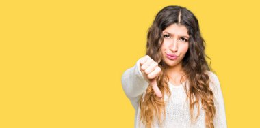 Mutsuz ve kızgın ret gösterilen ve başparmak aşağı hareketi ile negatif seyir beyaz kazak giyen genç güzel kadın. Kötü ifade.