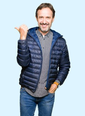 Orta yaş yakışıklı adam kış ceket giyiyor mutlu yüz görünümlü ve başparmak yukarı ile yan işaret gülümseyen.