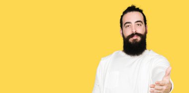 Uzun saç ve sakal tebrik ve konuksever dost sunan karşılıklı gülümseyen sportif sweatshirt giyen genç adam. Başarılı iş.