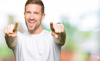 Olumlu ve neşeli gülümseyen casual beyaz t-shirt işaretleme ve parmaklar, kamerayla giyen yakışıklı adam