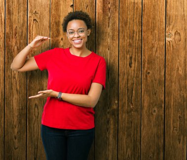 Büyük ve büyük boy işaret, ölçü birimi sembol gösteren ellerle eller izole arka plan üzerinde gözlük güzel genç Afro-Amerikan kadın. Kameraya bakarak gülümsüyordu. Ölçüm kavramı.