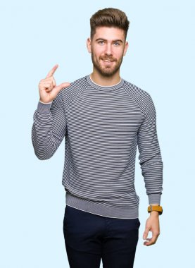Görünümlü çizgili kazak giyen genç yakışıklı adam ve kamera bakarken el parmaklar ile boyut işareti yapıyor ile gülümseyen ve emin işaret. Ölçü kavramı.