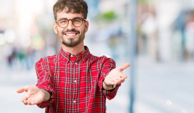 Sarılmak için kollarını açarak gülümseyerek kameraya bakarak izole arka plan üzerinde gözlük takan yakışıklı delikanlı. Neşeli ifade kucaklayan mutluluk.