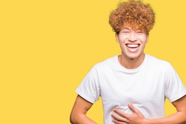 Genç yakışıklı adam ile afro saç giymek Casual beyaz t-shirt gülümseyen ve sert dışarı gülüyor Çünkü komik çılgın şaka. Mutlu ifade.