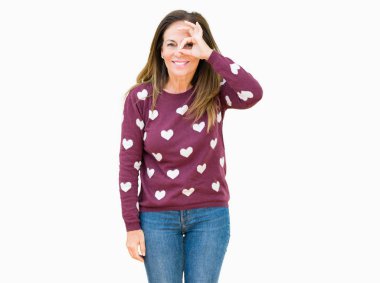 Güzel orta yaş kadın izole arka plan üzerinde kalpler kazak giyen el gülümseyerek ok jest yapıyor, mutlu yüz ile parmaklardan bakan göz.