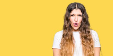 Genç güzel kadın rahat beyaz t-shirt korkuyor ve sürpriz ifade, korku ve heyecanlı yüz ile şok giyiyor.