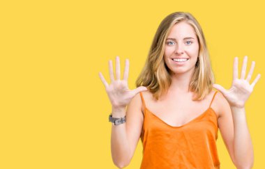 Gösterilen ve parmakları ile işaret izole arka plan üzerinde turuncu gömlek giymiş güzel genç kadın kendinden emin ve mutlu gülümseyerek süre on numara.