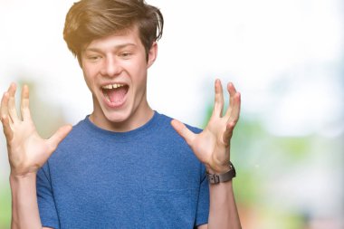 Genç yakışıklı adam izole arka plan üzerinde mavi t-shirt giyen deli kutluyor ve kollarını kaldırdı ve açık gözleri heyecan çığlık ile başarı için hayran. Kazanan kavramı