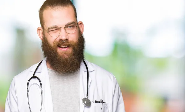 Joven Médico Rubio Con Barba Con Abrigo Médico Guiñando Ojo — Foto de Stock