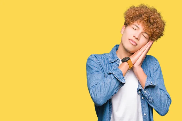 Young handsome man with afro hair wearing denim jacket sleeping tired dreaming and posing with hands together while smiling with closed eyes.