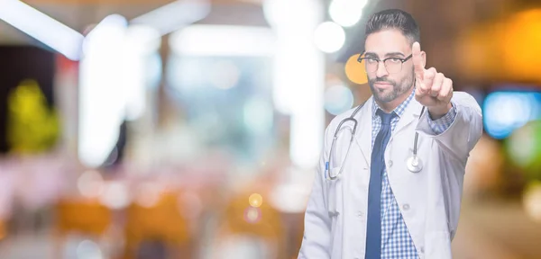 Handsome young doctor man over isolated background Pointing with finger up and angry expression