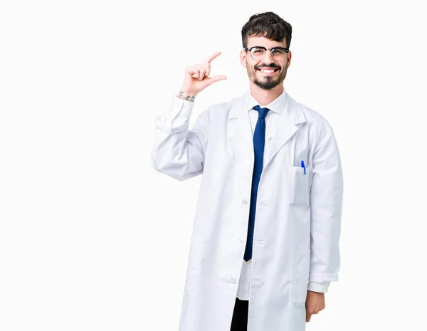 年轻的专业科学家男子穿着白色外套在孤立的背景微笑和自信地手势与手做大小标志用手指 同时看和照相机 测量概念 — 图库照片
