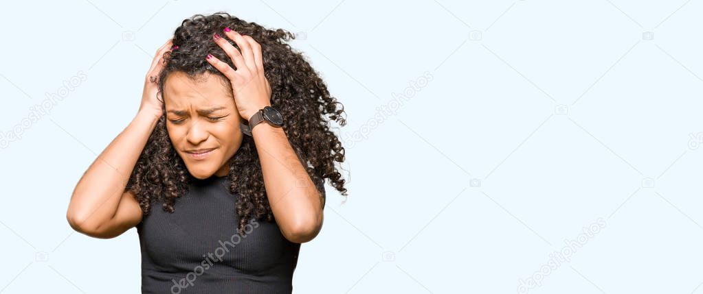 Young beautiful woman with curly hair suffering from headache desperate and stressed because pain and migraine. Hands on head.