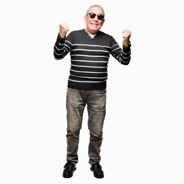 Kış kazak ve güneş gözlüğü giyen yakışıklı kıdemli adam şaşırttı ve silah yükseltilmiş ve açık gözleri ile başarı için hayran kutluyor. Kazanan kavramı.